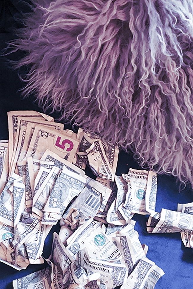 Image shows a pile of crumpled dollar bills next to a fluffy lavendar pillow.