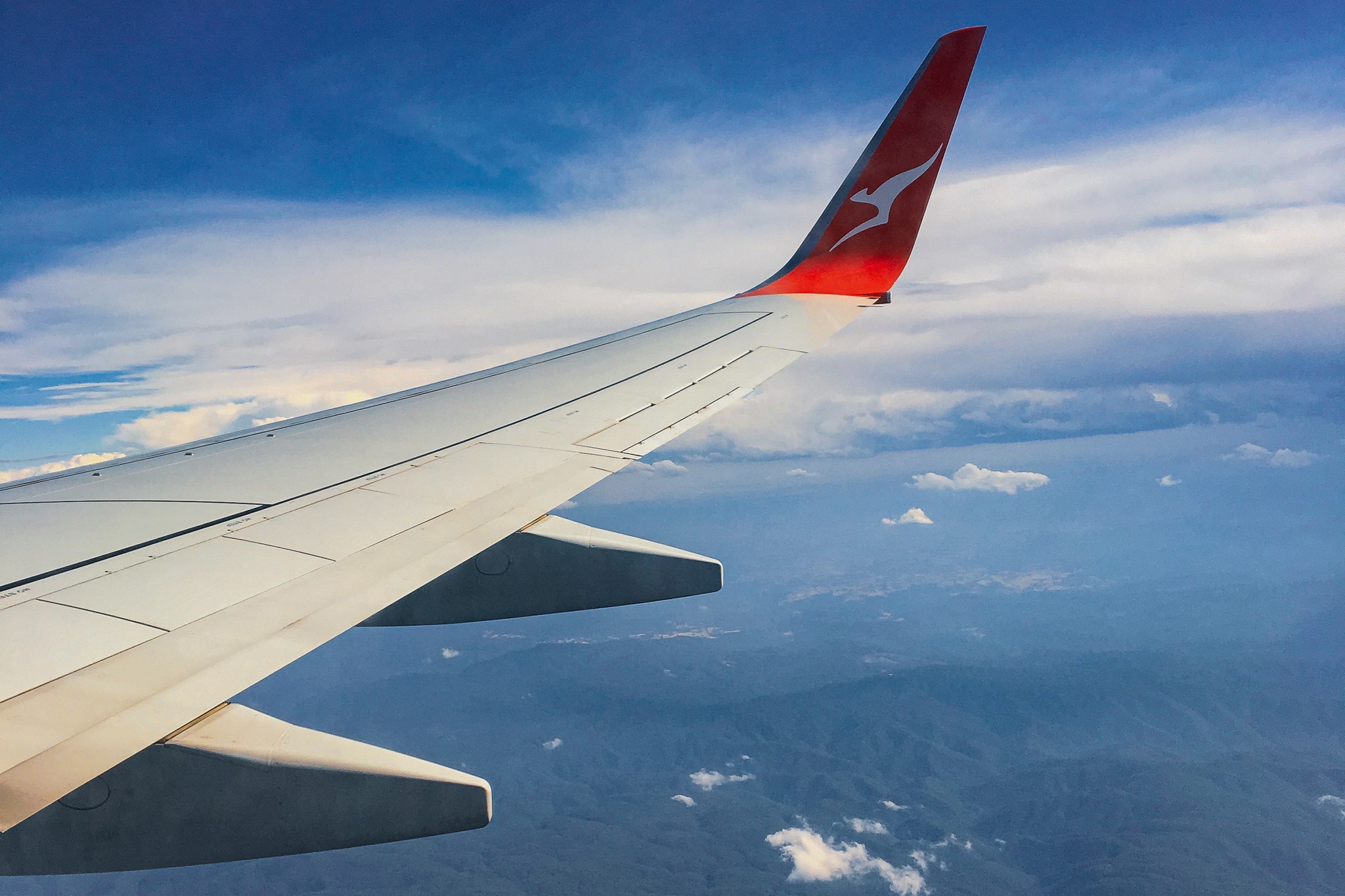 Image shows the view of liftoff from an airlplane window seat. Clouds are visible above craggy green mountains.