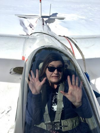 Jezebel is sitting in a single seat airplane cockpit in a tiny plane, and pressing her hands against the glass like she is trapped.